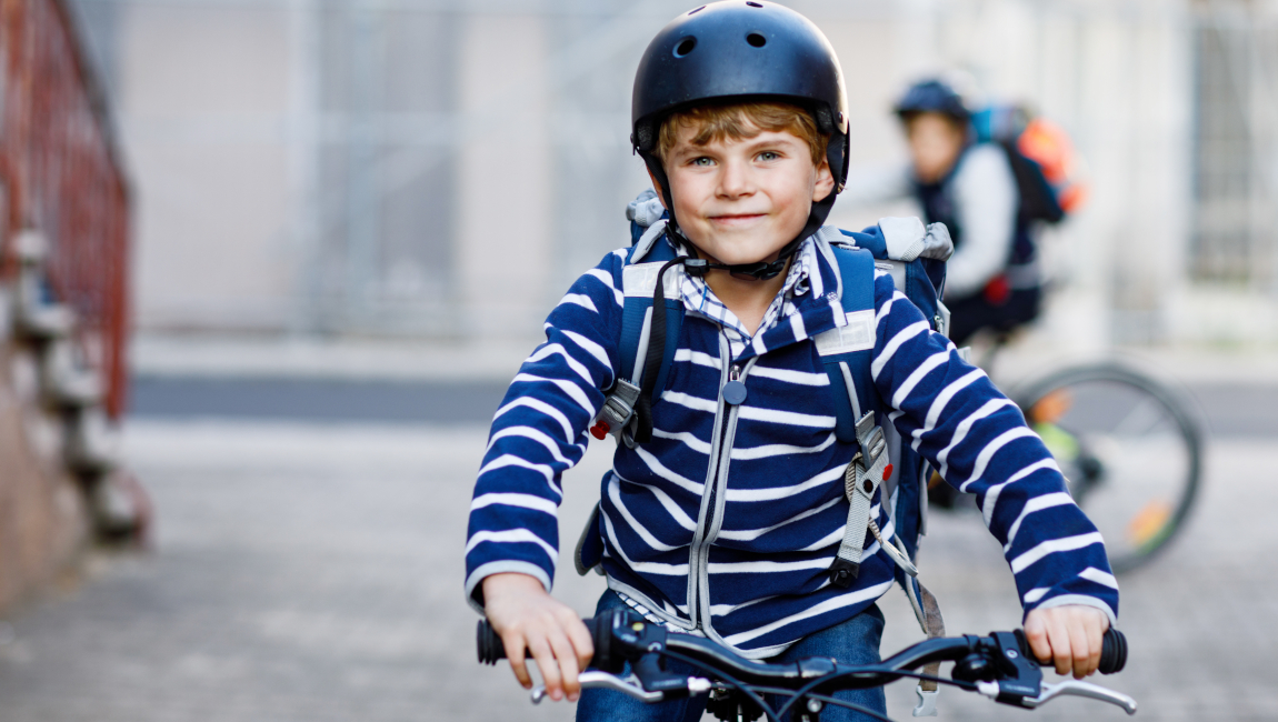 Zwei Schuljungen mit Schutzhelm fahren mit dem Fahrrad in der Stadt mit Rucksäcken.