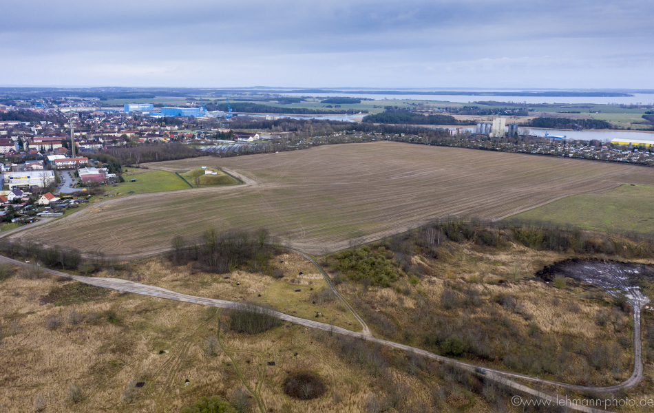 Blick von oben auf ein großes Feld. Im Vordergrund sind befestigte Wege und im Hintergrund eine Stadt.