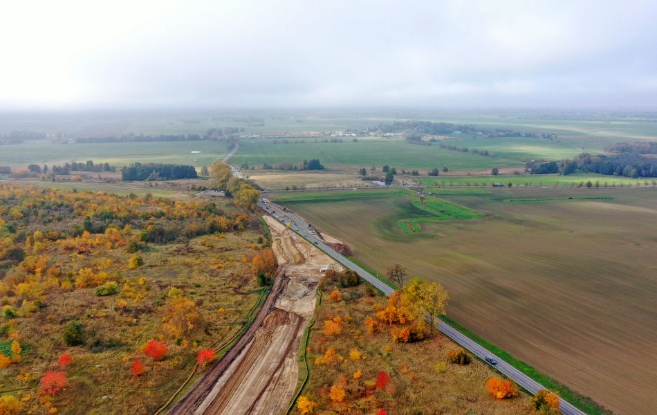 Eine Trasse aus Erde führt durch ein Wäldchen und mündet in einer vielbefahrenen Straße, der B 111. Im Hintergrund sind mehrere Felder.