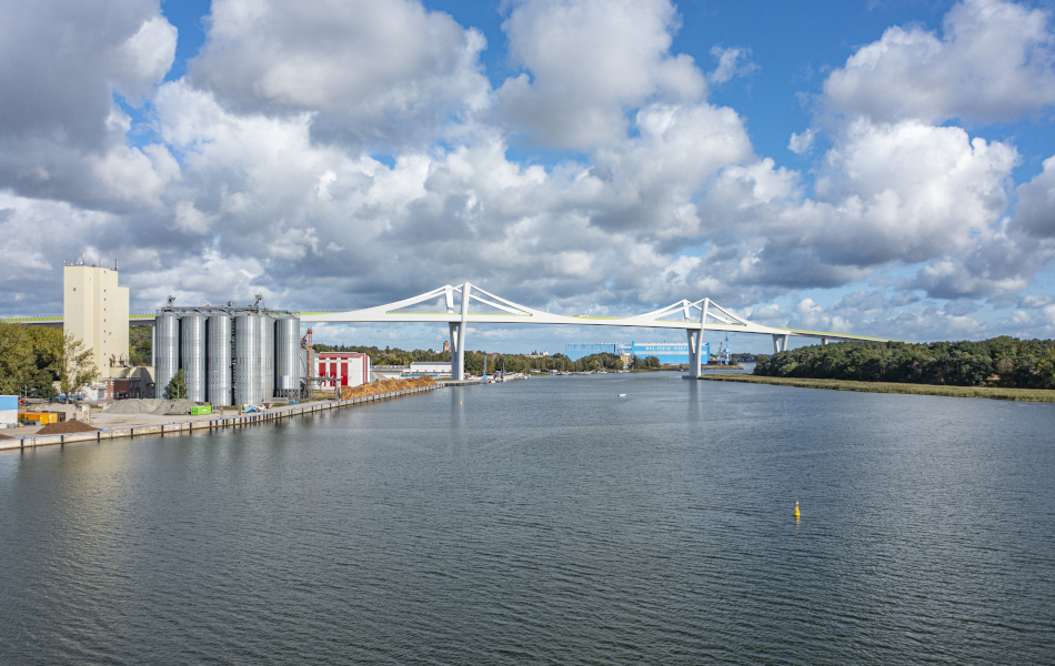 Über ein Gewässer, die Peene, führt eine Brücke mit zwei Pylonen. Auf der linken Uferseite stehen Silos, auf der rechten Bäume. Im Hintergrund ist die Werft.