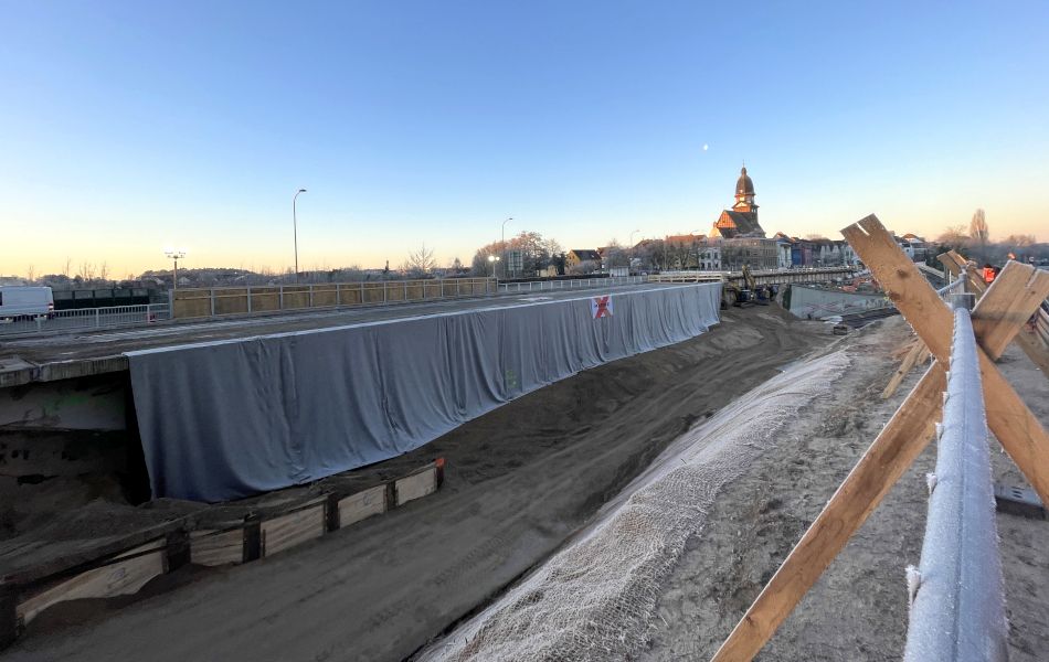 Auf einer Brücke hängt ein riesiger, grauer Vorhang erhunter. Im Hintergrund sind eine Kirche, Häuser und der Mond.