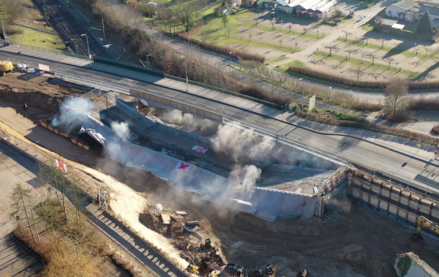 Zwei Straßenbrücke führen über Bahngleise. Die vordere Straßenbrücke ist eingestürzt und es bilden sich Rauchwolken. 