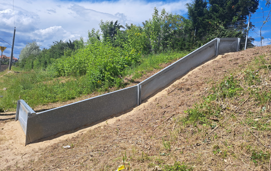 Auf einem Hang steht ein Zaun aus Beton quer von unten nach oben.