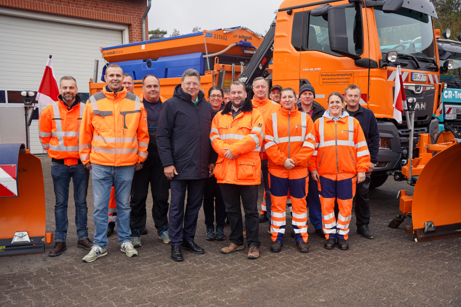 Gruppenfoto in der Straßenmeisterei Kröpelin: Mecklenburg-Vorpommerns Wirtschafts- und Infrastrukturminister Reinhard Meyer steht zusammen mit den Straßenwärtern vor der Fahrzeughalle und den Einsatzfahrzeugen der Straßenmeisterei.