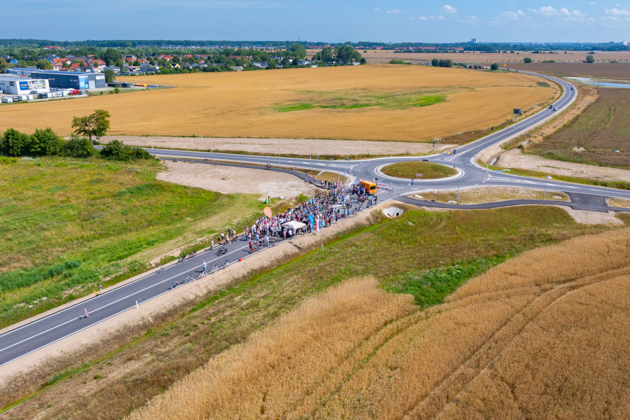 Viele Menschen stehen auf einer neuen Straße. Sie feiern die Eröffnung. Die Straße führt zu einem neuen Kreisverkehr auf dem Land. © Pixelbox15 Viele Menschen stehen auf einer neuen Straße. Sie feiern die Eröffnung. Die Straße führt zu einem neuen Kreisverkehr auf dem Land.